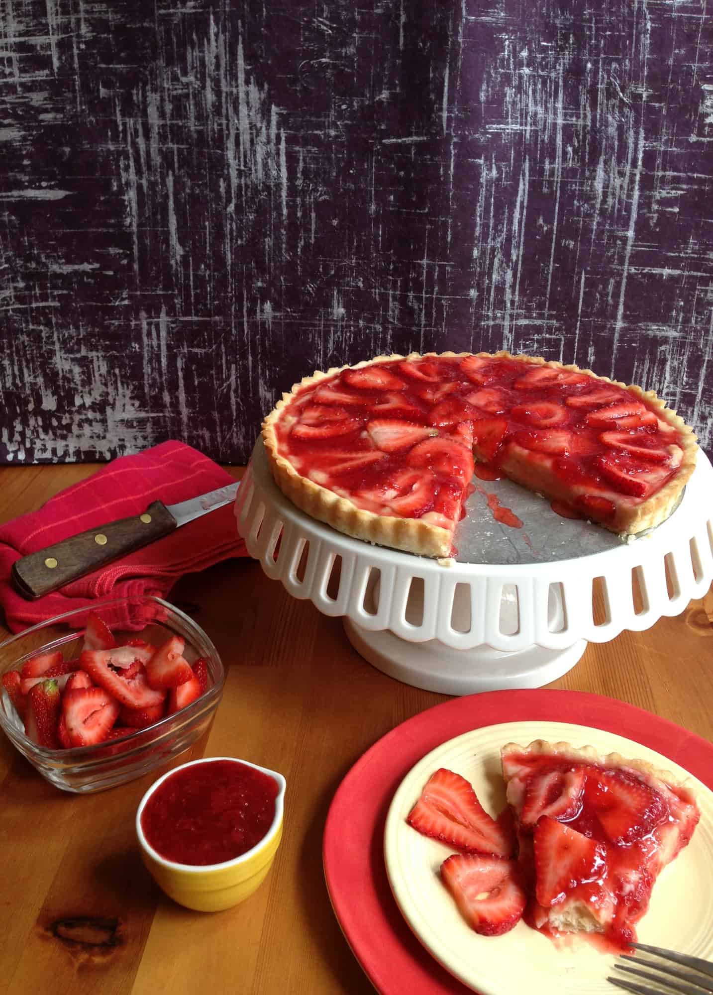 rustic strawberry french tart on a table with slice on plate. 