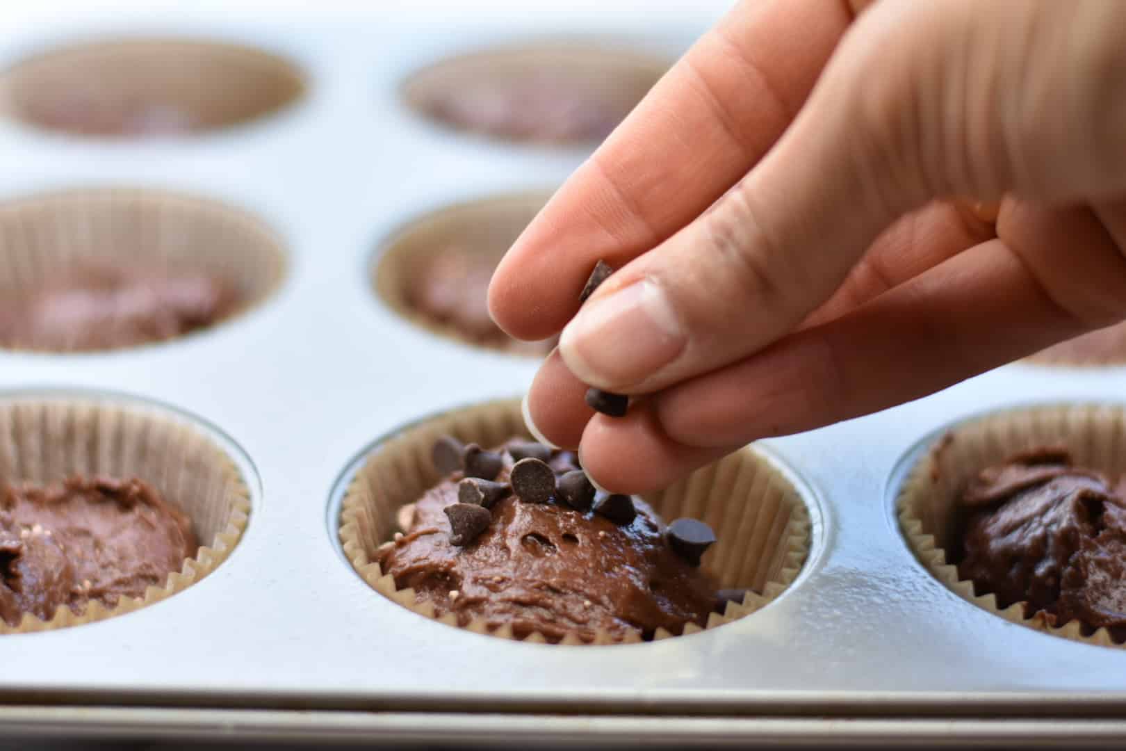 closeup of hand sprinkling chocolate chips on muffins