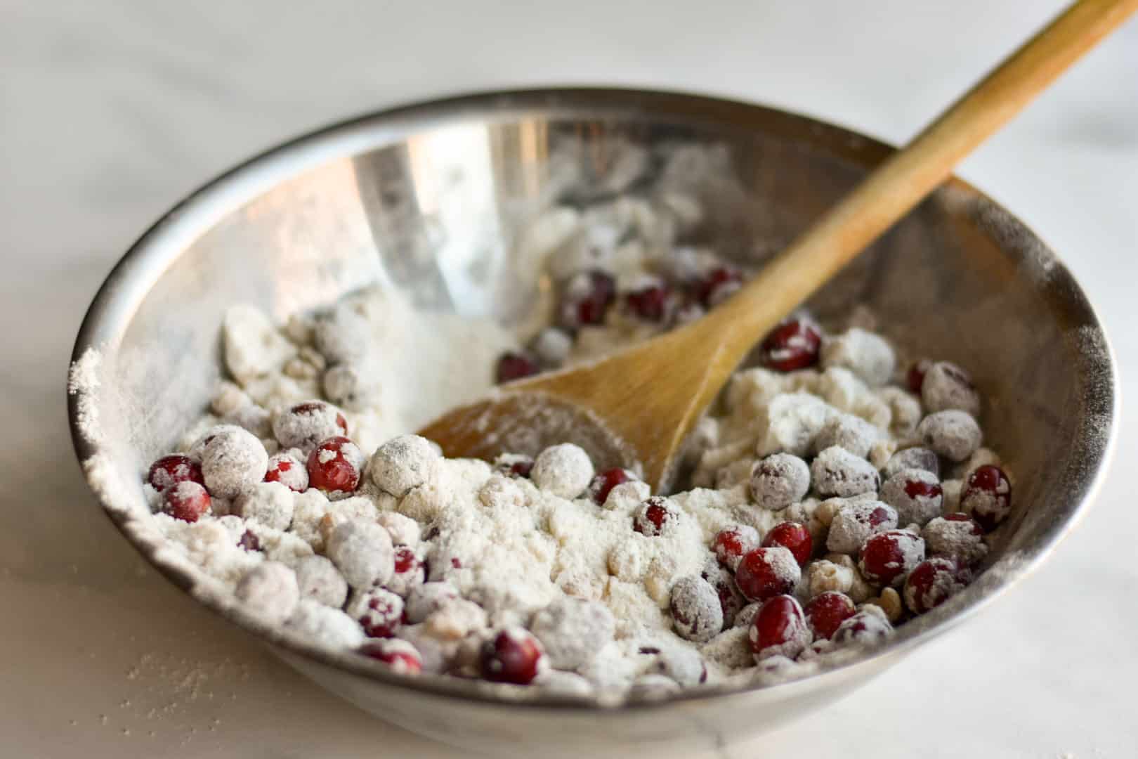 dry ingredients and cranberries in bowl with wooden spoon