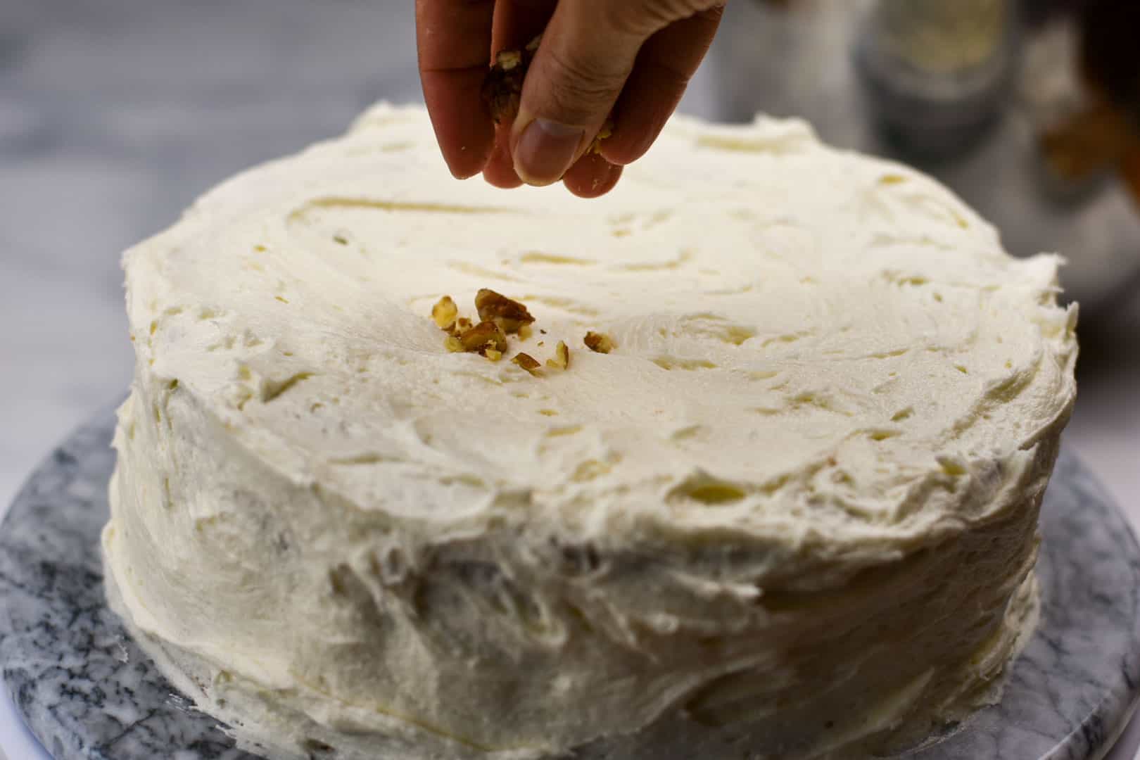 closeup of hand sprinkling pecans on the top of the cake