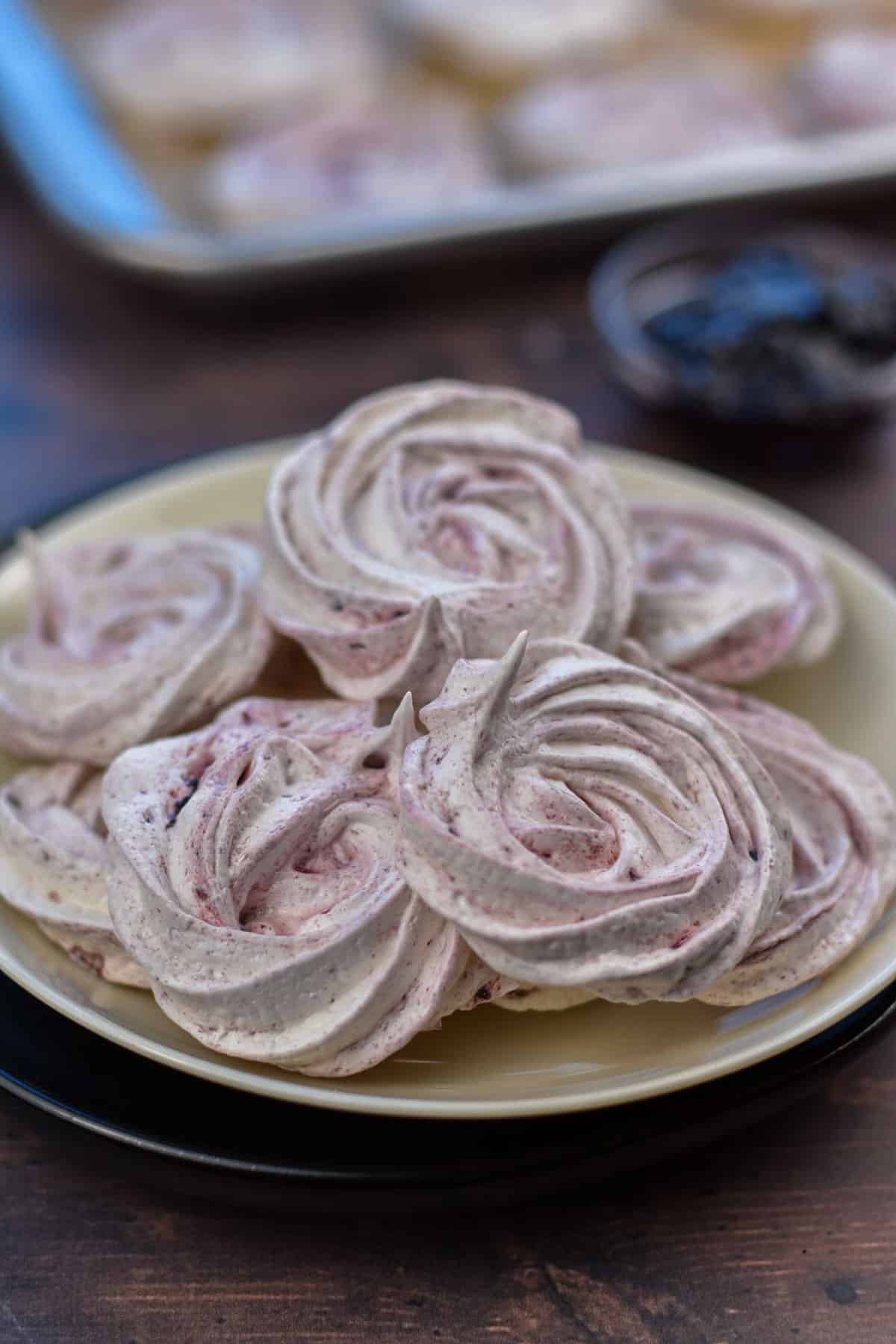 meringue cookies on a plate with blackberry jam in the background.