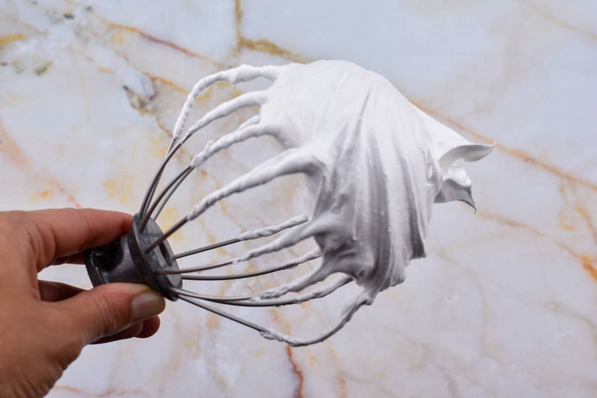 hand holding whisk attachment with french meringue stiff peaks