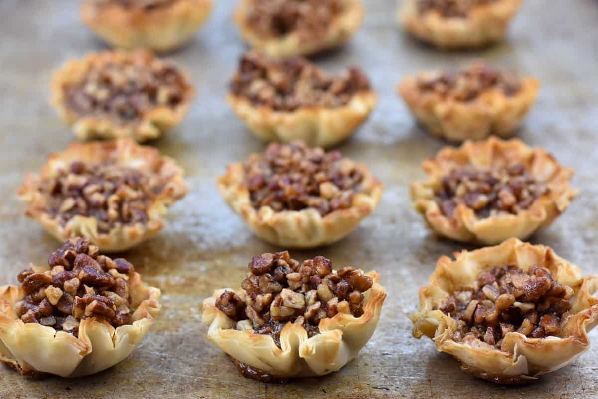mini pecan tarts lined up on a baking sheet.