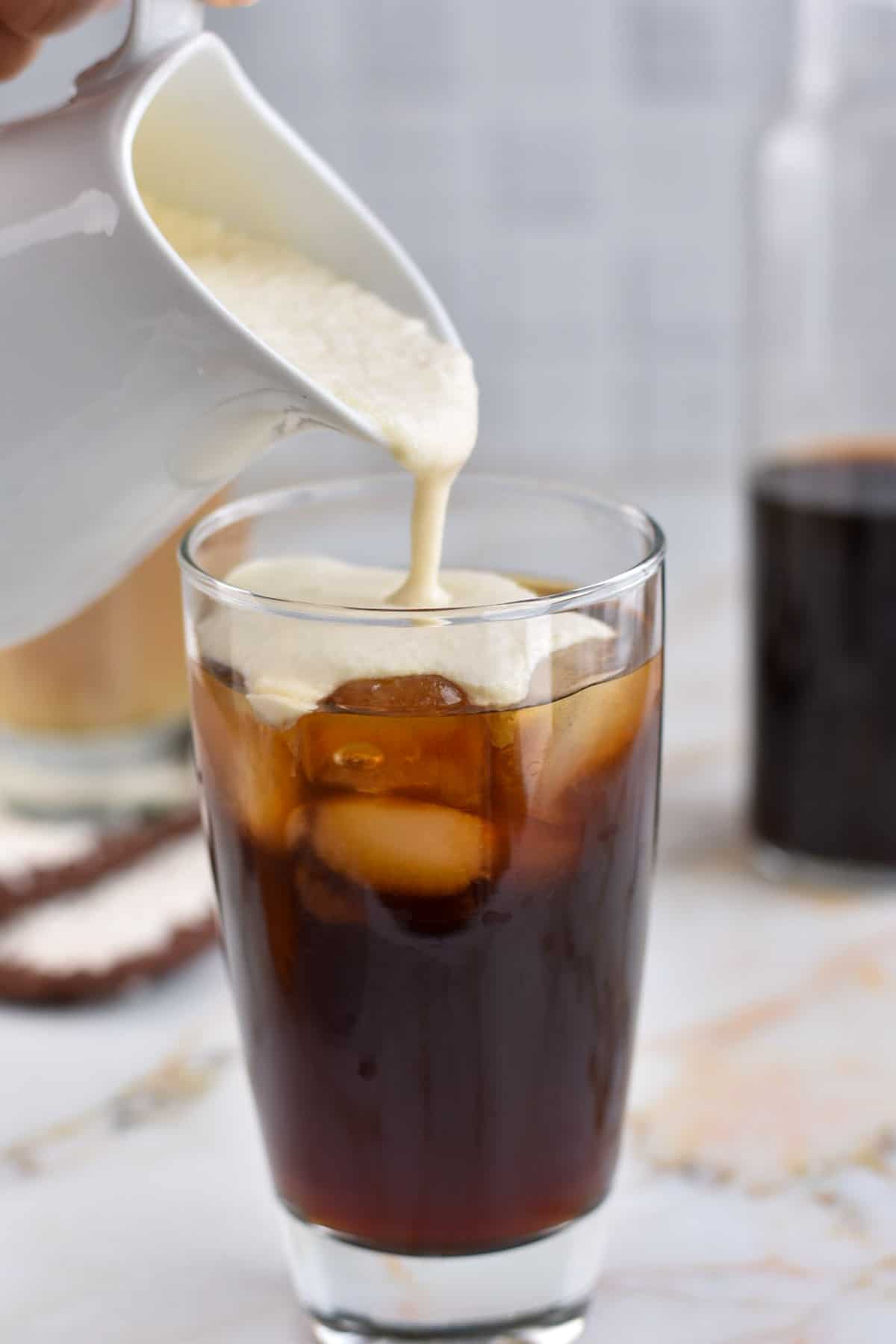 irish cream being pouring into cold brew coffee in a clear glass