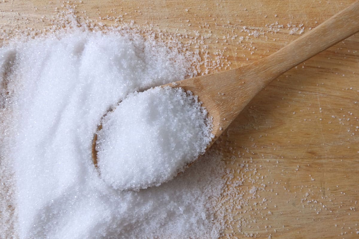 granulated salt in a spoon on wooden counter
