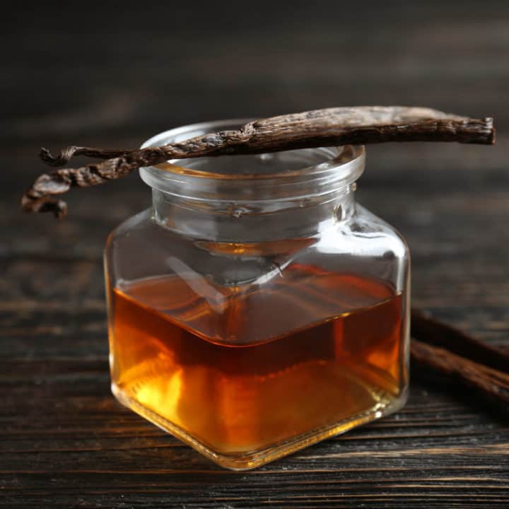 vanilla extract in a clear jar with vanilla bean on top.