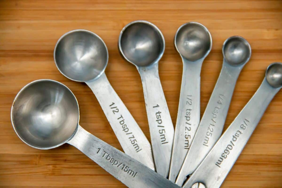 Six metal measuring spoons, labeled from 1 tablespoon to ⅛ teaspoon, are fanned out on a wooden surface—perfect for learning how to measure ¾ teaspoon with accuracy and ease.