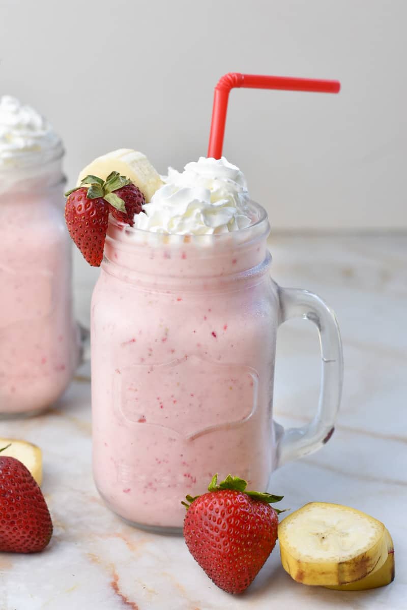 strawberry milkshake in glass with whipped cream and banana garnish. 