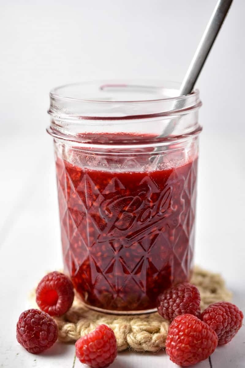 clear cup with compote and raspberries on counter.