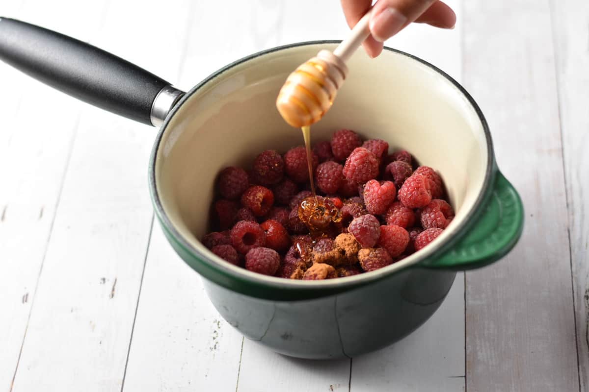 honey being drizzled into pot of raspberries.