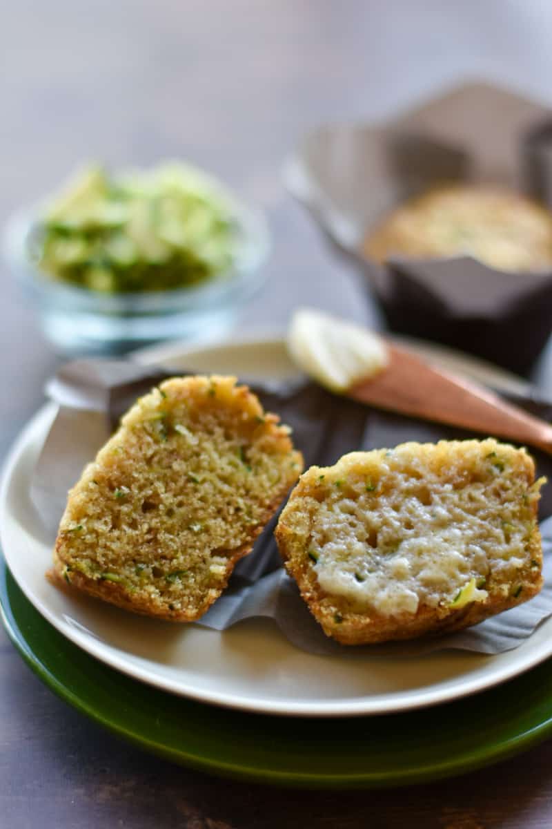 zucchini applesauce muffins on a white plate with butter.