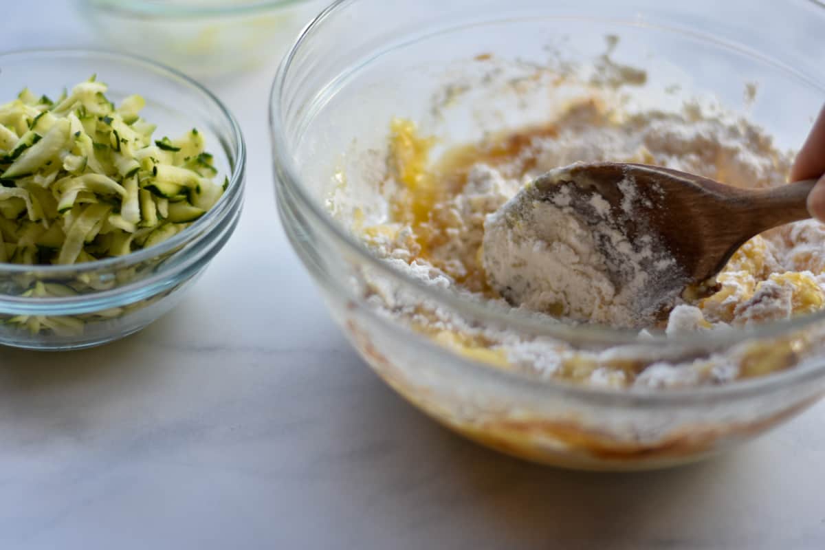 wooden spoon mixing flour with applesauce in glass bowl.