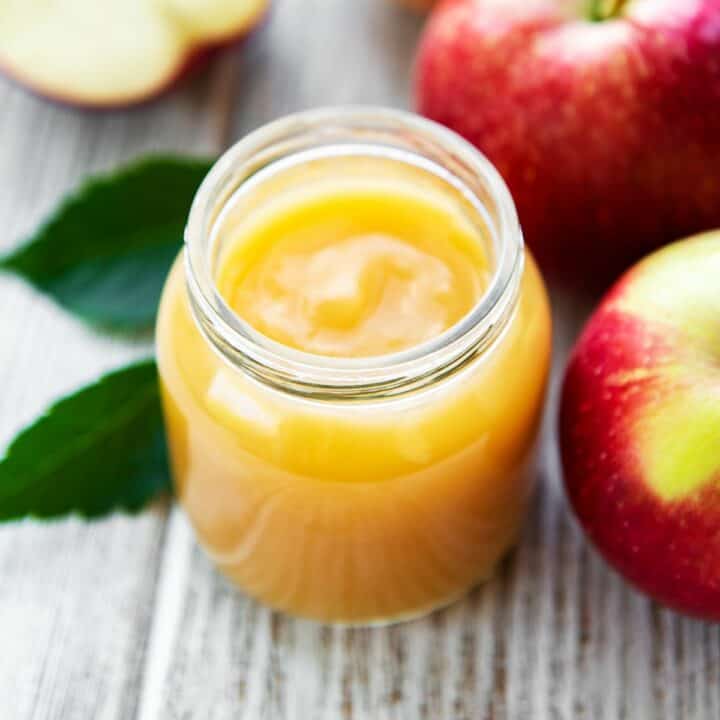 applesauce in a glass jar with apples in background.
