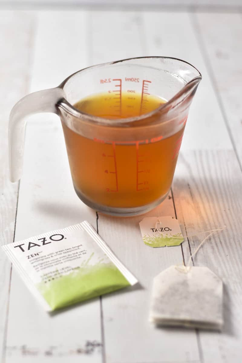 green tea steeping in a measuring cup with a tea bag on counter.