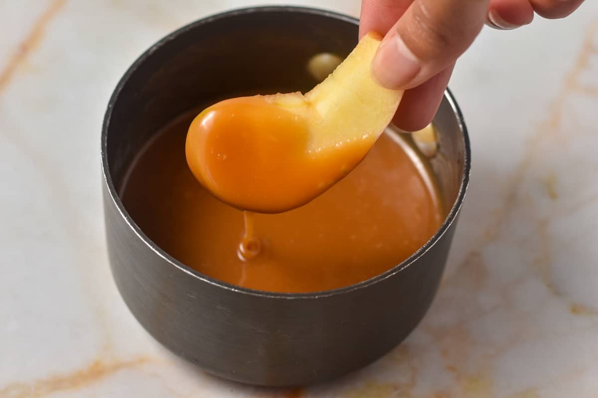 hand dipping apple into hot caramel in a pot.