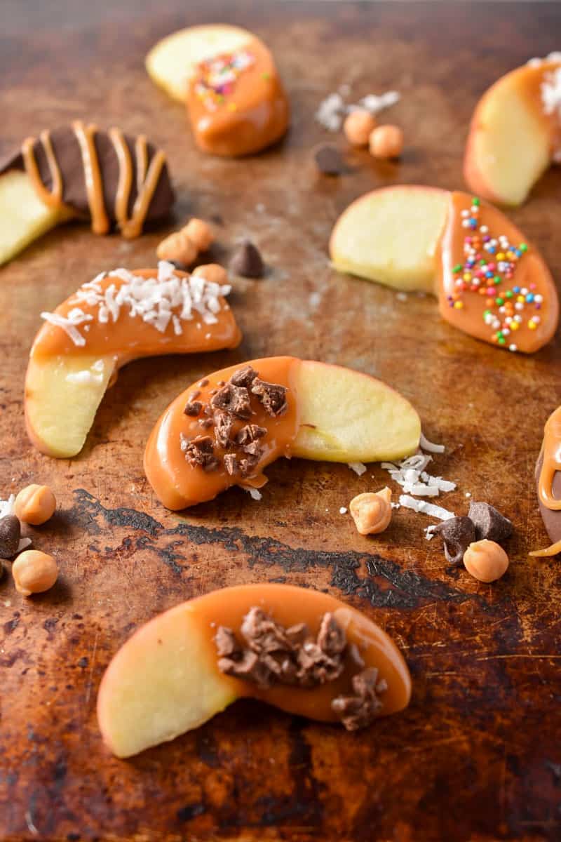 caramel apple slices on the counter with toppings.