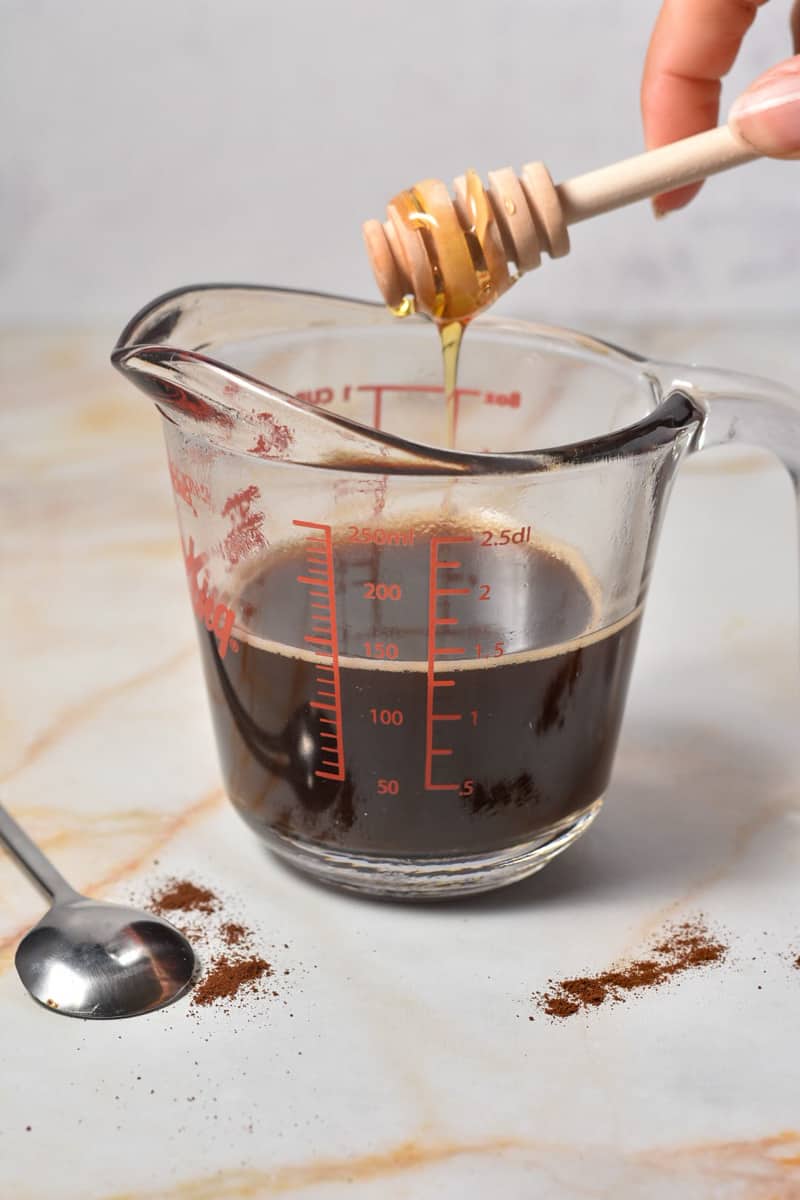 brewed espresso in a measuring cup with honey being drizzled in.