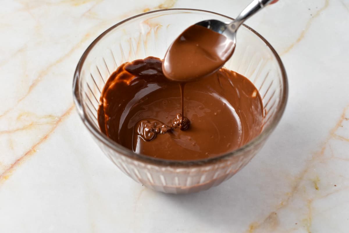 melted chocolate in a clear bowl with a spoon and drizzling chocolate.