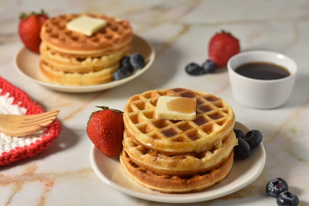 three waffles stacked on a plate with butter.