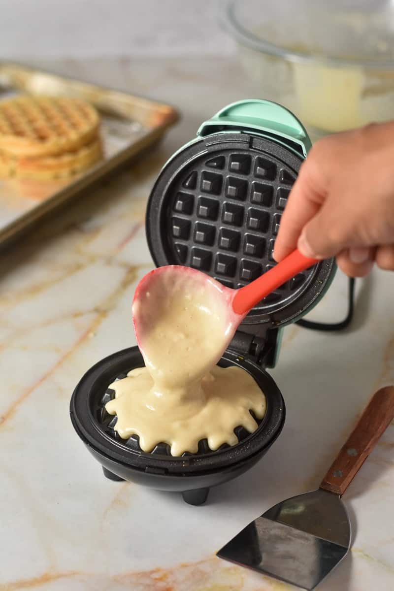 spooning batter into mini waffle maker.