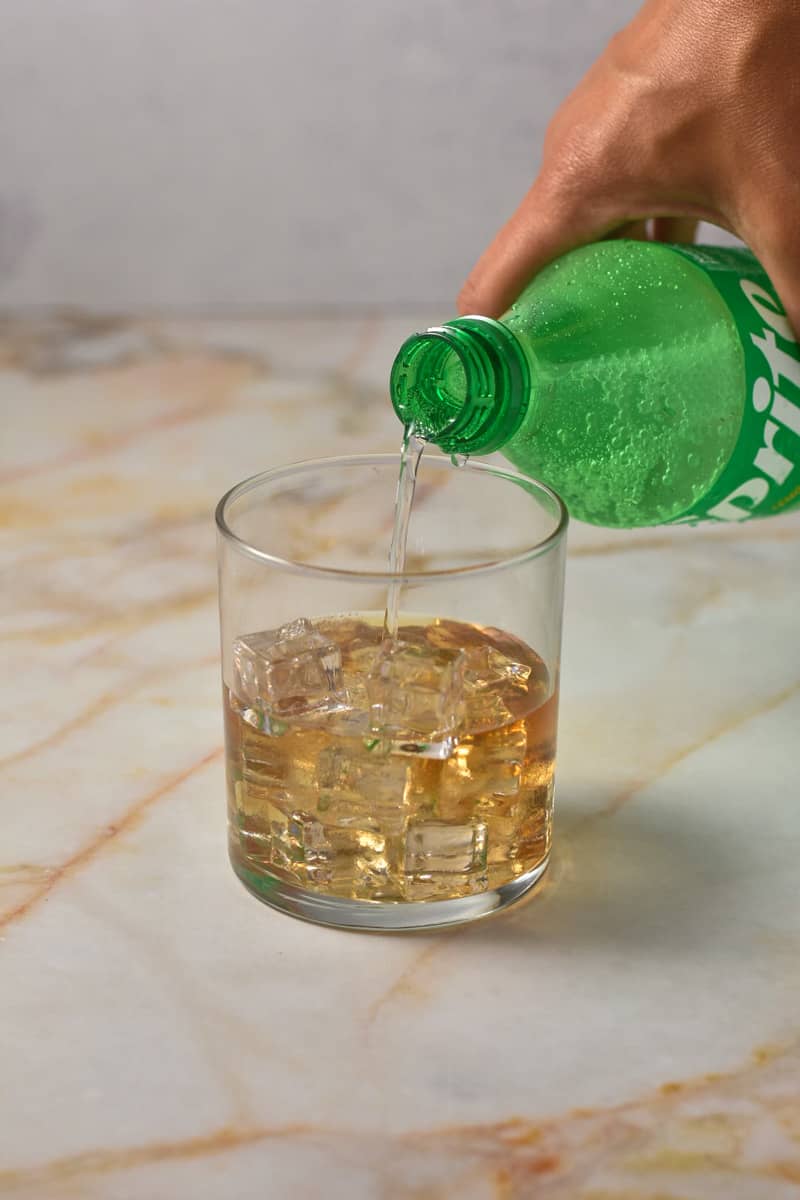 hand pouring sprite into glass with crown apple.