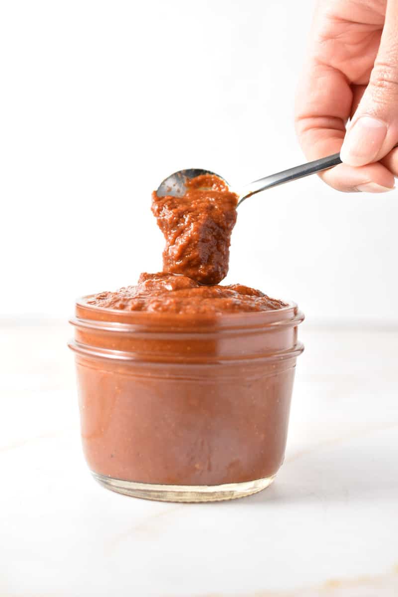 spoon with tex mex paste dripping into a clear glass container filled with sauce.