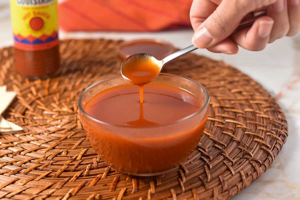 spoon dipped into popeye's sweet heat sauce in a bowl. 