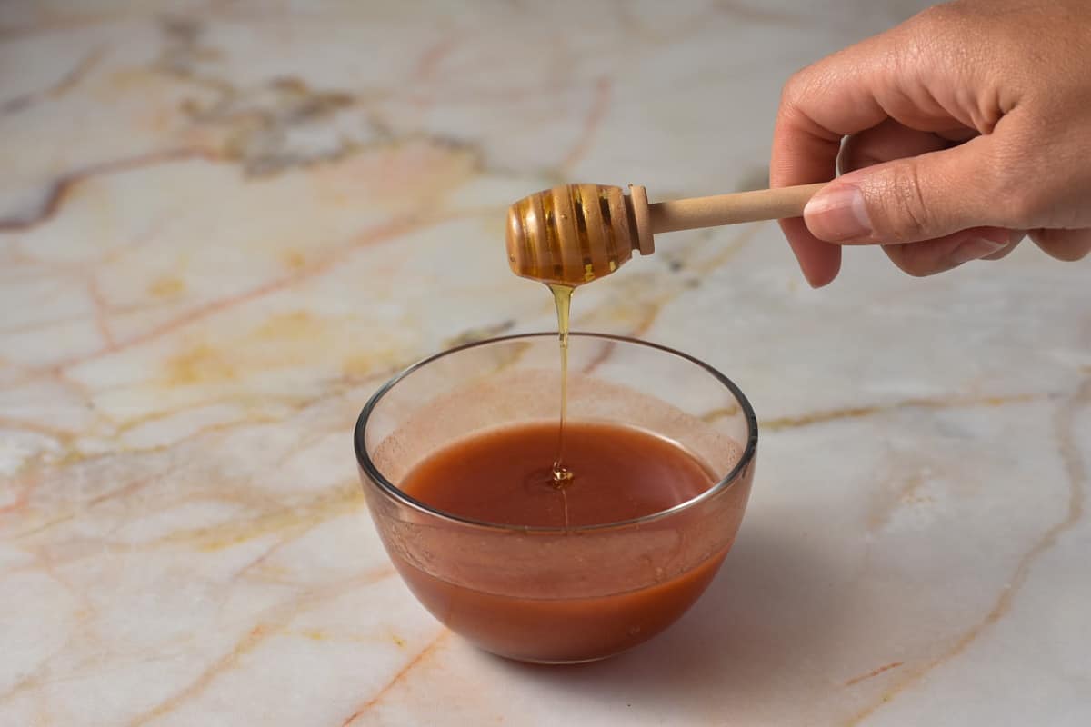 honey being poured into small glass bowl with sugar and hot sauce. 