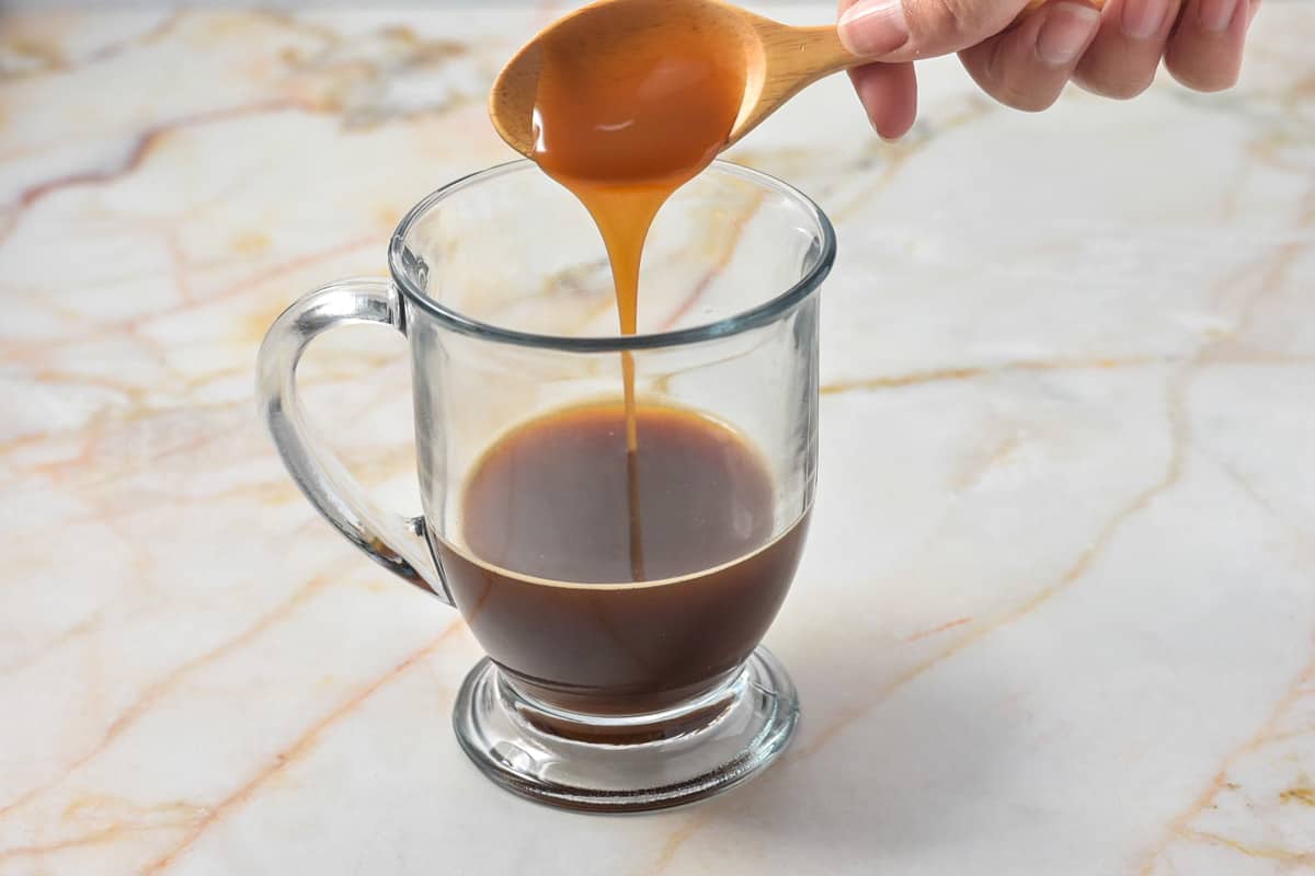 pouring caramel sauce into clear coffee mug with espresso. 