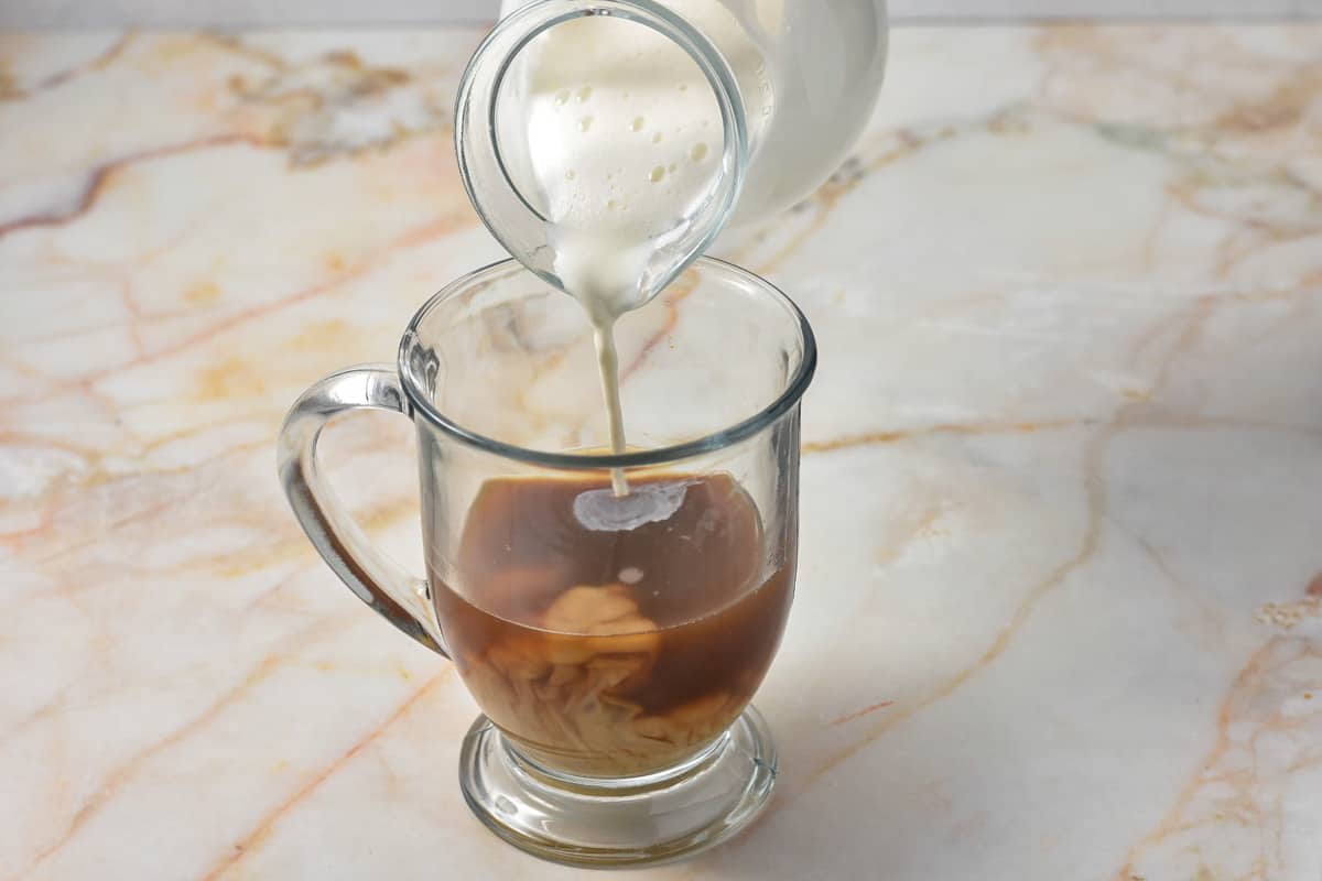pouring half and half into coffee mug with caramel sauce and espresso. 