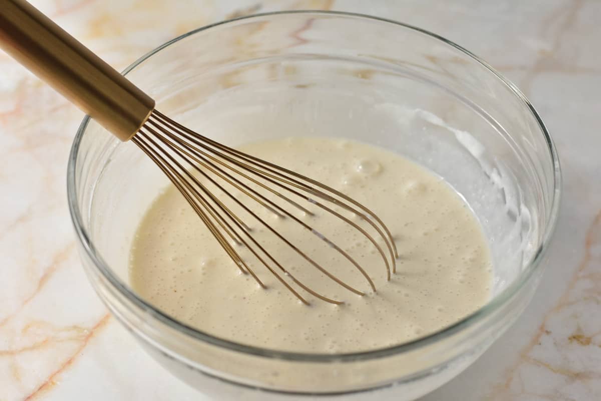 condensed milk, yogurt, and milk in a glass bowl with a metal whisk.