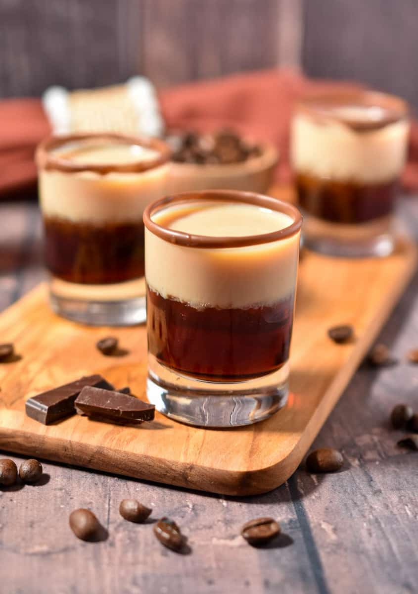shot glass filled and sitting on a wooden counter with coffee beans and chocolate.