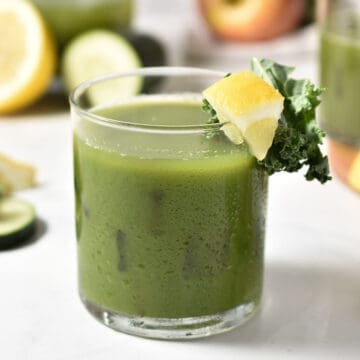 green juice in clear glass with lemon and kale garnish.