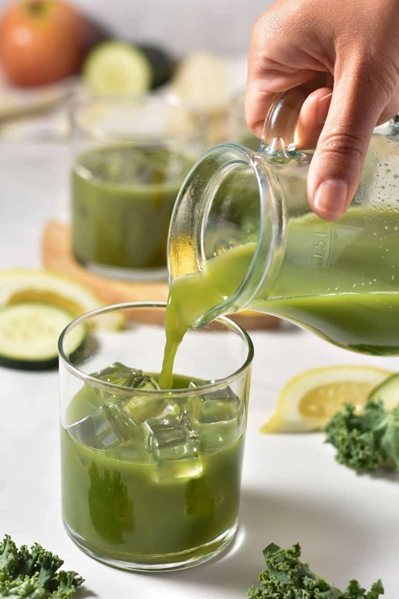 pouring green juice into a clear glass container.