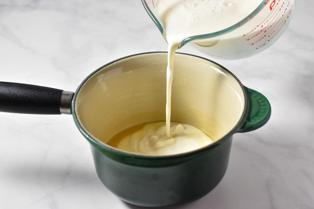 milk being poured into a roux of butter and flour in a pan.