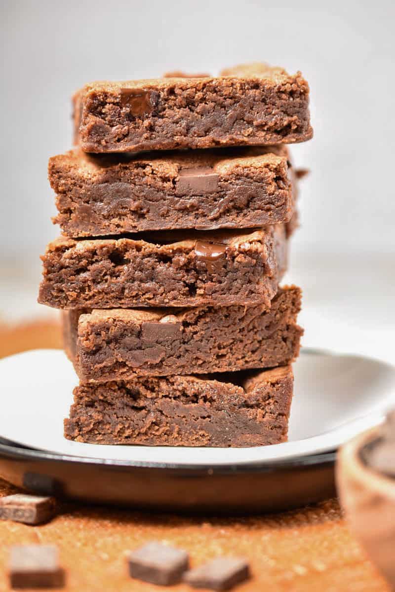 five chocolate brownies stacked high on a plate. 