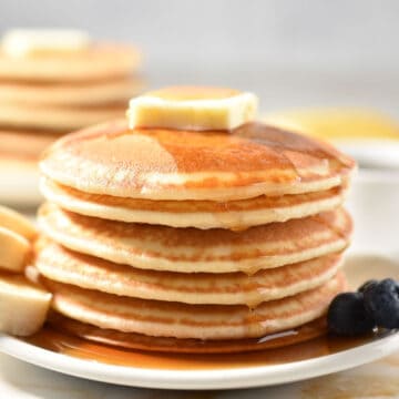 stack of six pancakes on a plate dripping with syrup and a pat of butter.