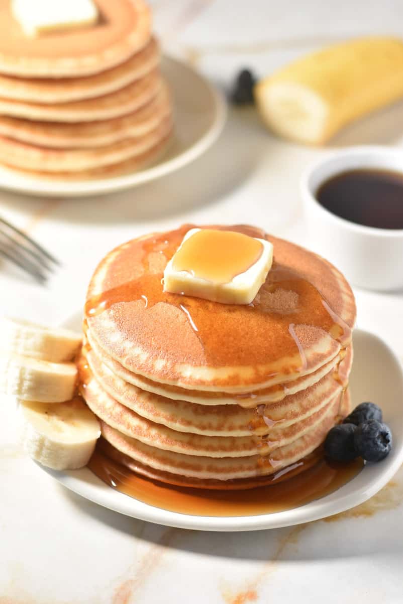 stack of pancakes on plate with pat of butter and syrup. 