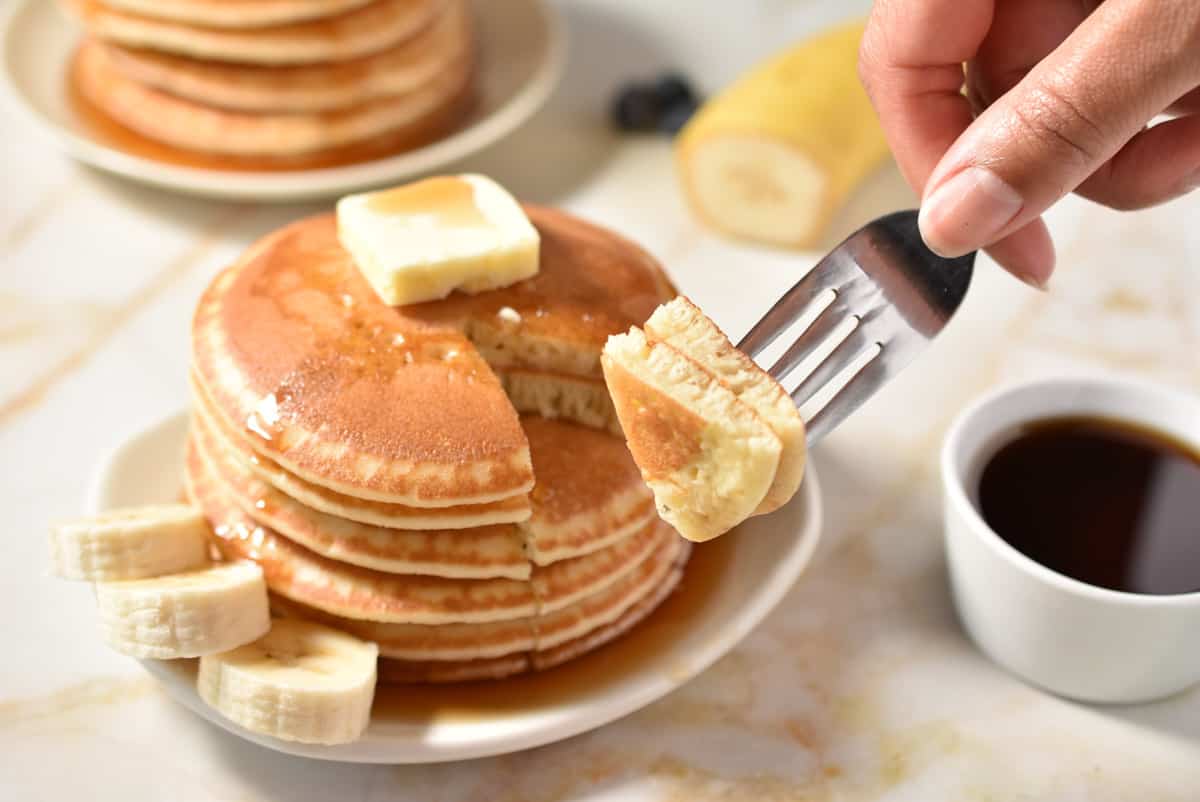 fork holding a bite of pancakes with larger stack in the background. 