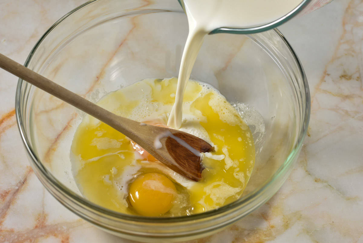 eggs and butter in a bowl, with milk being poured in over the top. 