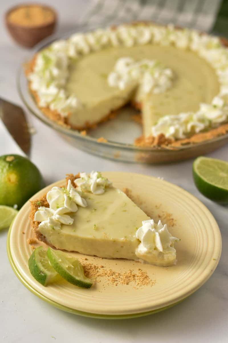 slice of key lime pie on a plate with lime wedges and whipped cream.