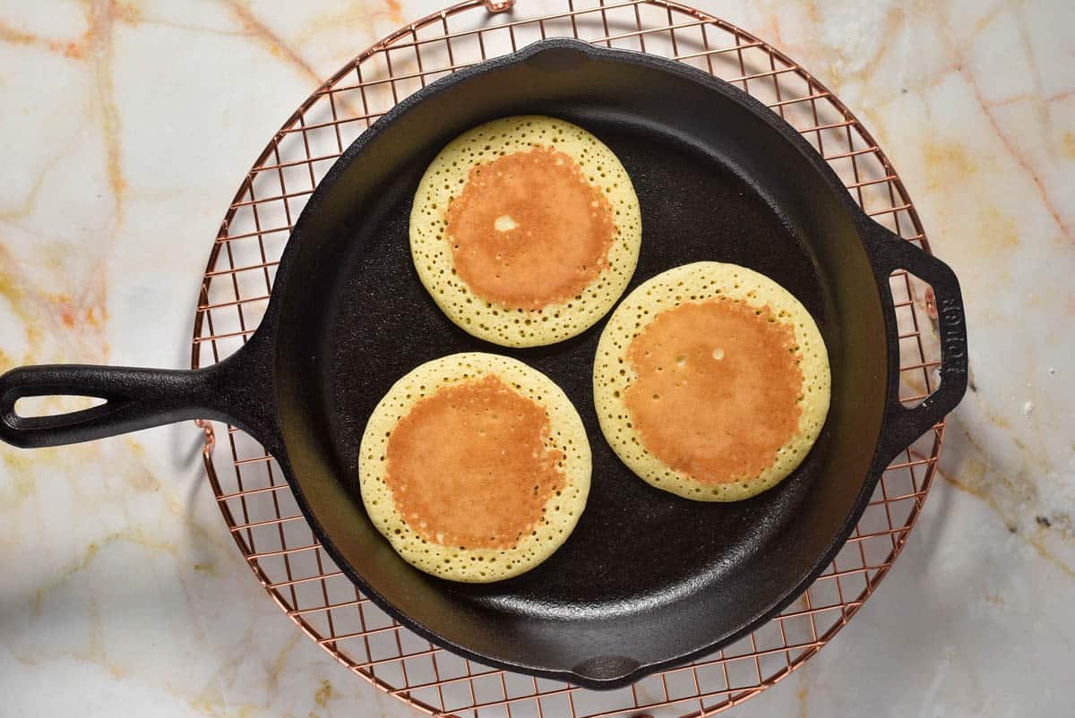 three pancakes cooking in a cast iron skillet. 