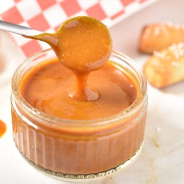 honey gold sauce in a bowl with a spoon ladling the sauce.