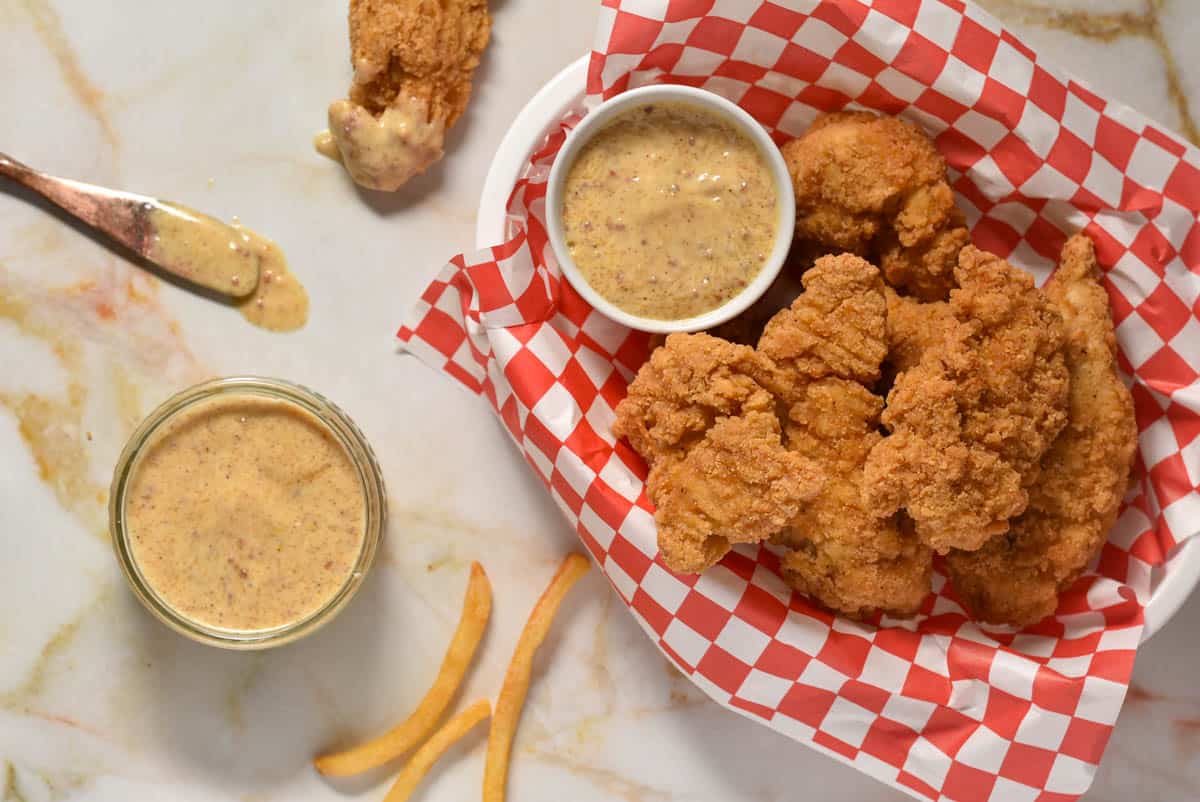 basket of chicken tenders and two bowls of popeye;s mardi gras mustard.