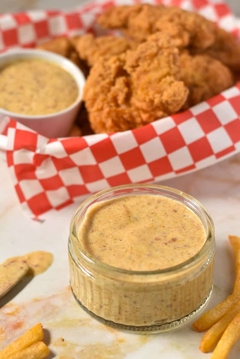 mustard dipping sauce in a bowl with a basket of chicken tenders and french fries.