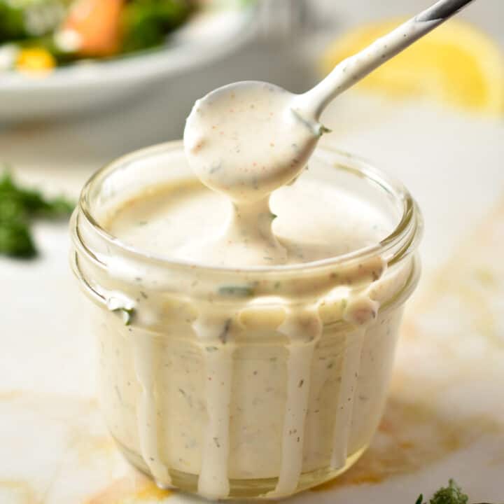 creamy ranch dressing dripping off a spoon in a cup.
