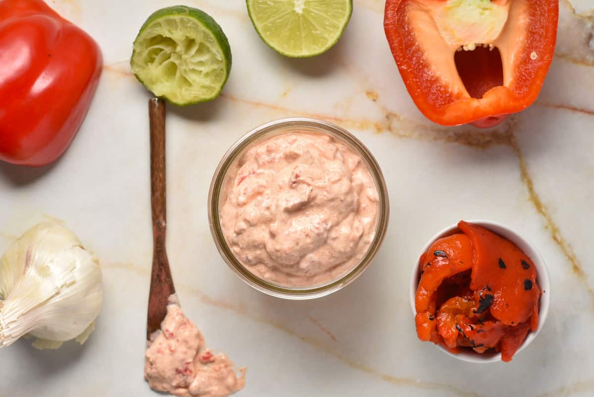 red pepper crema on a counter with roasted peppers, garlic, and limes. 