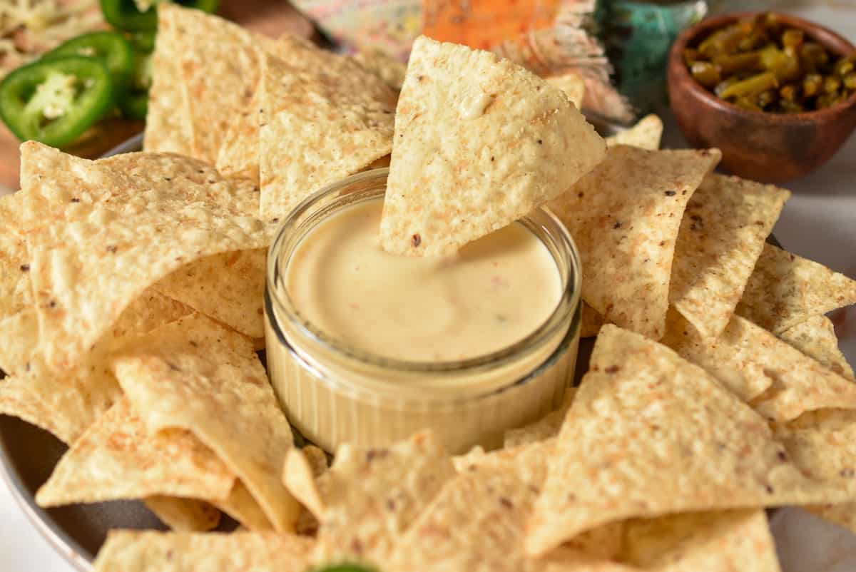 a small bowl with homemade queso. a tortilla chip is dipped in the queso. 