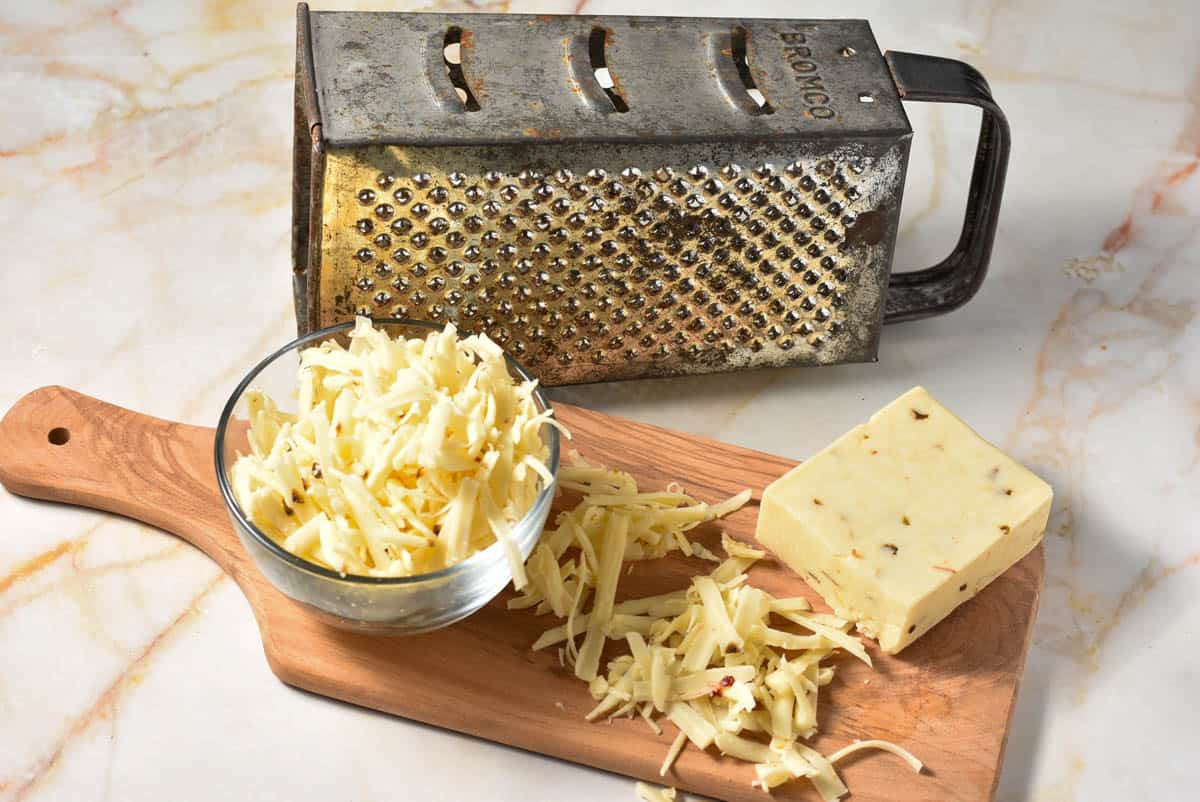 shredded pepper jack cheese on a wooden cutting board with a block of cheese. 