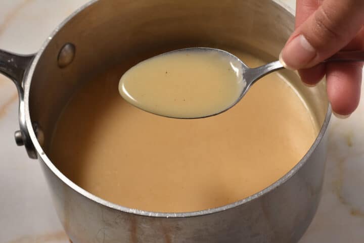 a spoon with gravy being held over a pot.